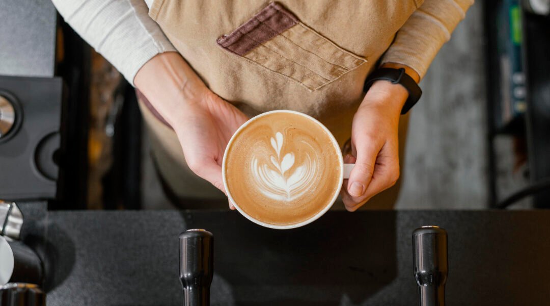 Barista de Che-Ka sosteniendo un café con latte art preparado con café de grano molido, mostrando textura y crema perfecta.
